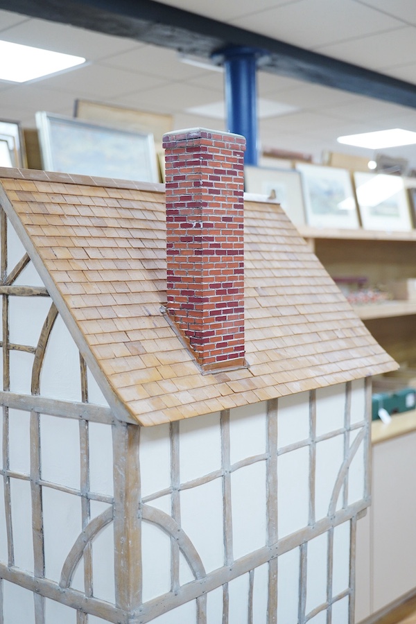 A modern doll’s house in the form of an oak framed Tudor house on three floors, with a shop on the ground floor, removable front panels on each floor and one side of the roof, with internal detailing and a good selection